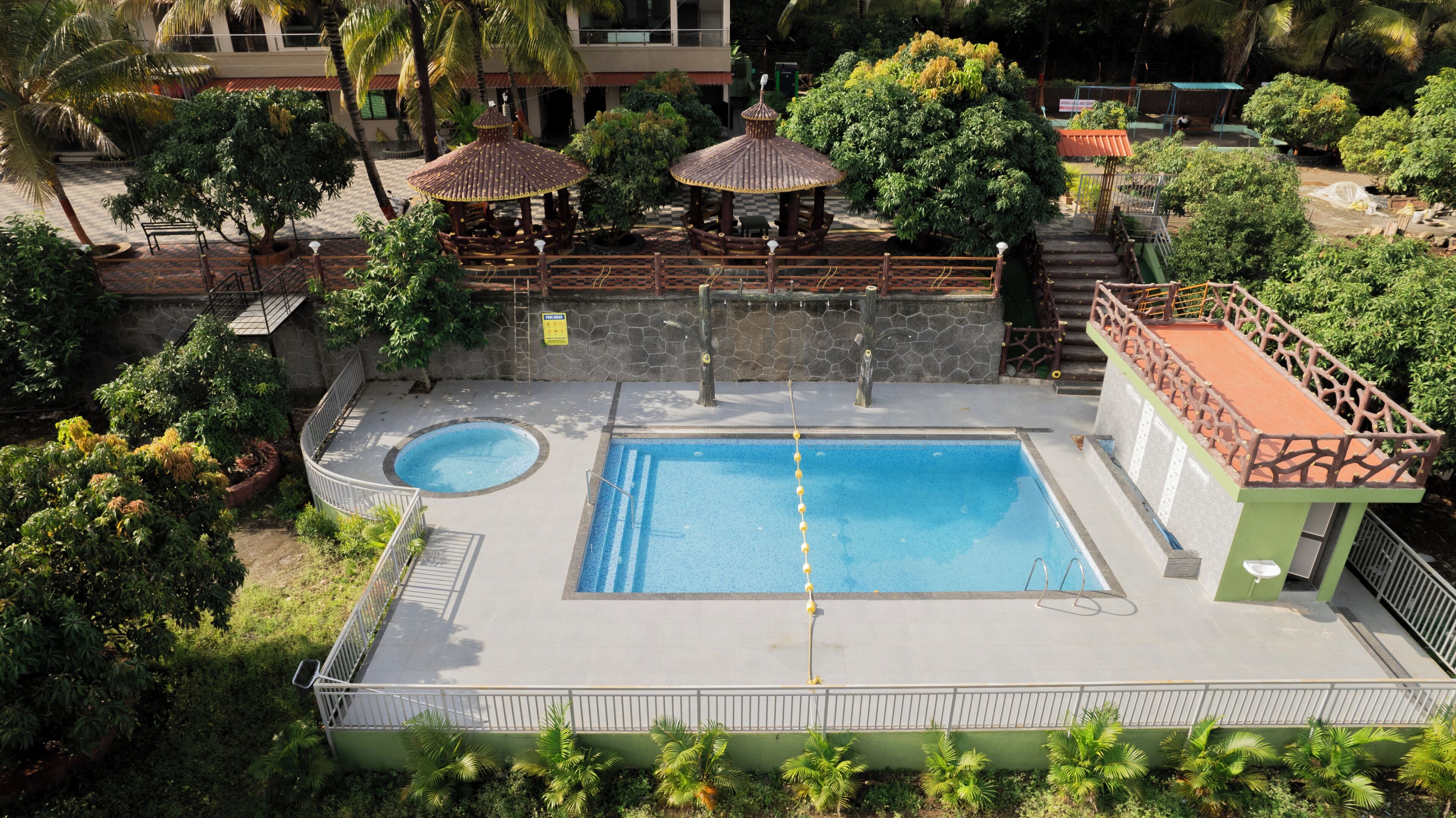 A rooftop pool with a small adjacent pool, surrounded by lush greenery and a gazebo.