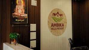 A reception area with a poster, a sign for Ambika Hills Resort, a plant, and a desk with a phone. - Ambika Hills Resort (Junnar)