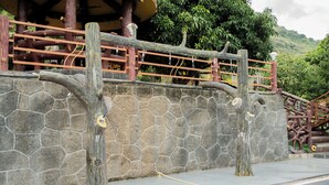 A stone wall with wooden tree-like structures and a rope barrier near a swimming pool. - Ambika Hills Resort (Junnar)