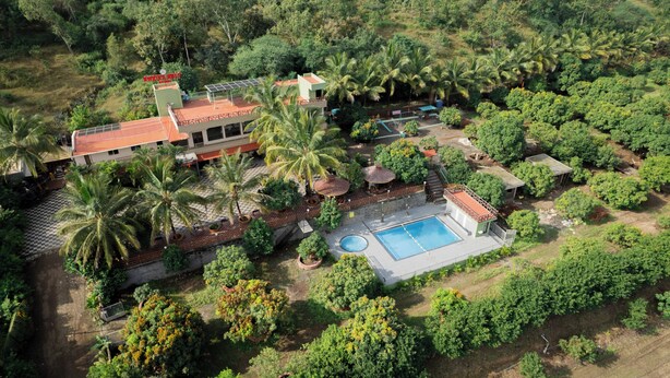 An aerial view of a property with a swimming pool, multiple buildings, and lush greenery. - Ambika Hills Resort (Junnar)