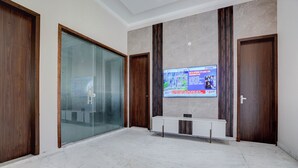 A spacious lobby with a marble floor, wooden doors, a glass partition, and a television displaying news. - Nirvana Hotel & Banquet (Batala)