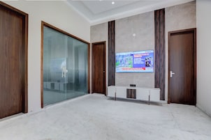 Un vestíbulo amplio con suelo de mármol, puertas de madera, una partición de vidrio y un televisor mostrando noticias.