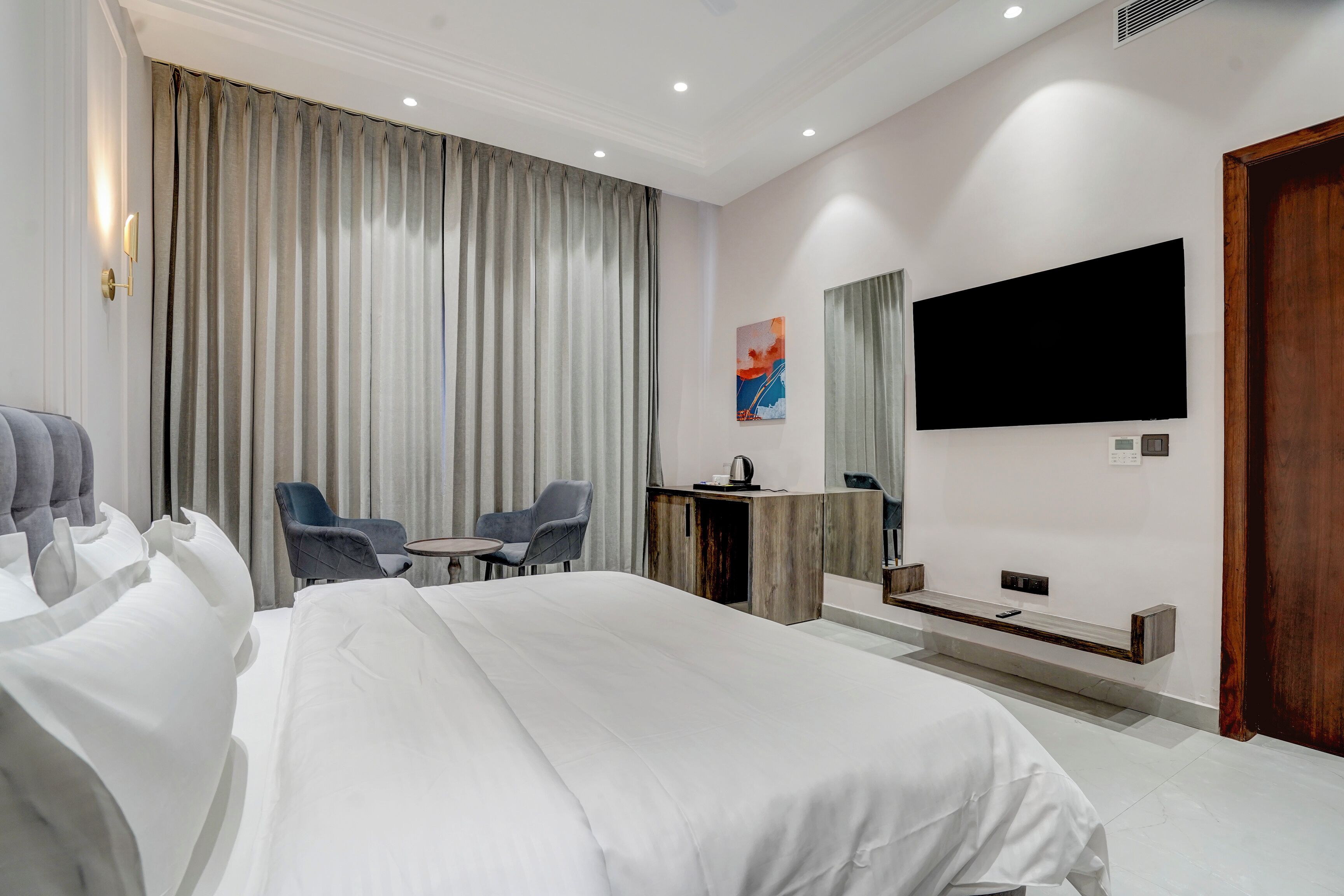 Hotelkamer met een groot bed, een bureau met stoel, een flatscreen televisie en een groot raam met gordijnen.