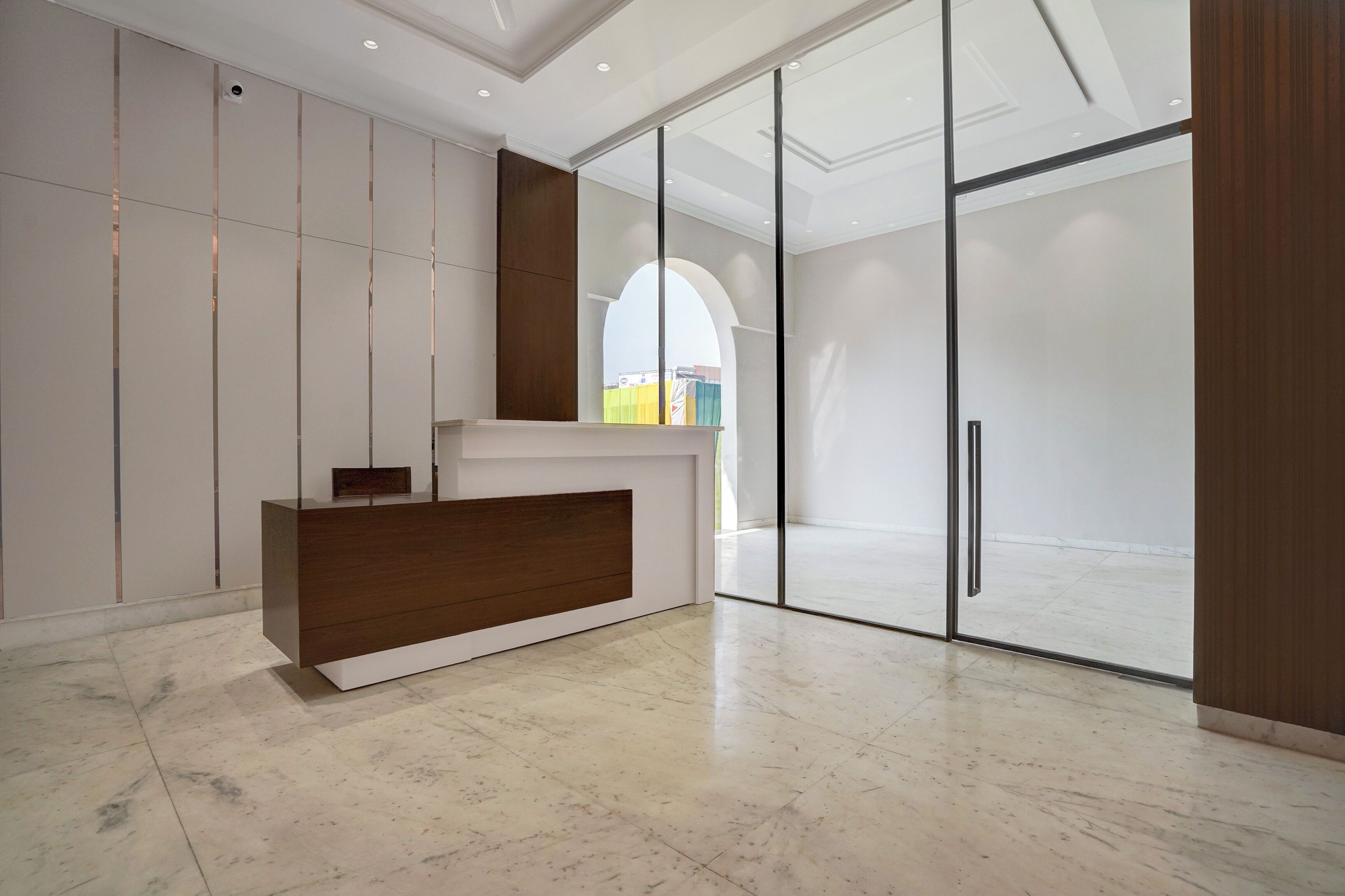 Una moderna zona de recepción con un mostrador de madera, una puerta de cristal grande que da al exterior y vistas del exterior a través del cristal.