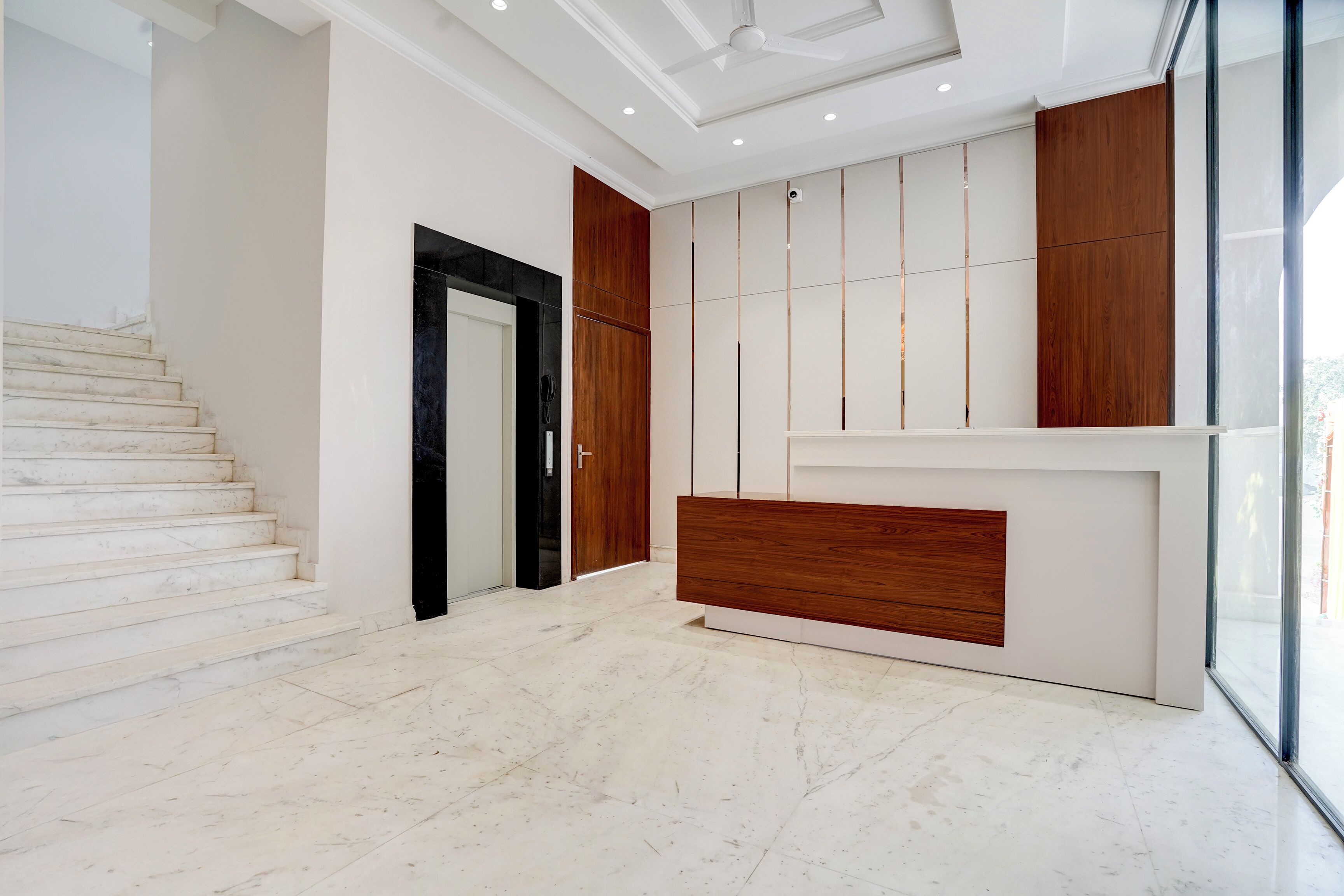 Interior moderno com escadaria de mármore, balcão de recepção e uma grande janela.
