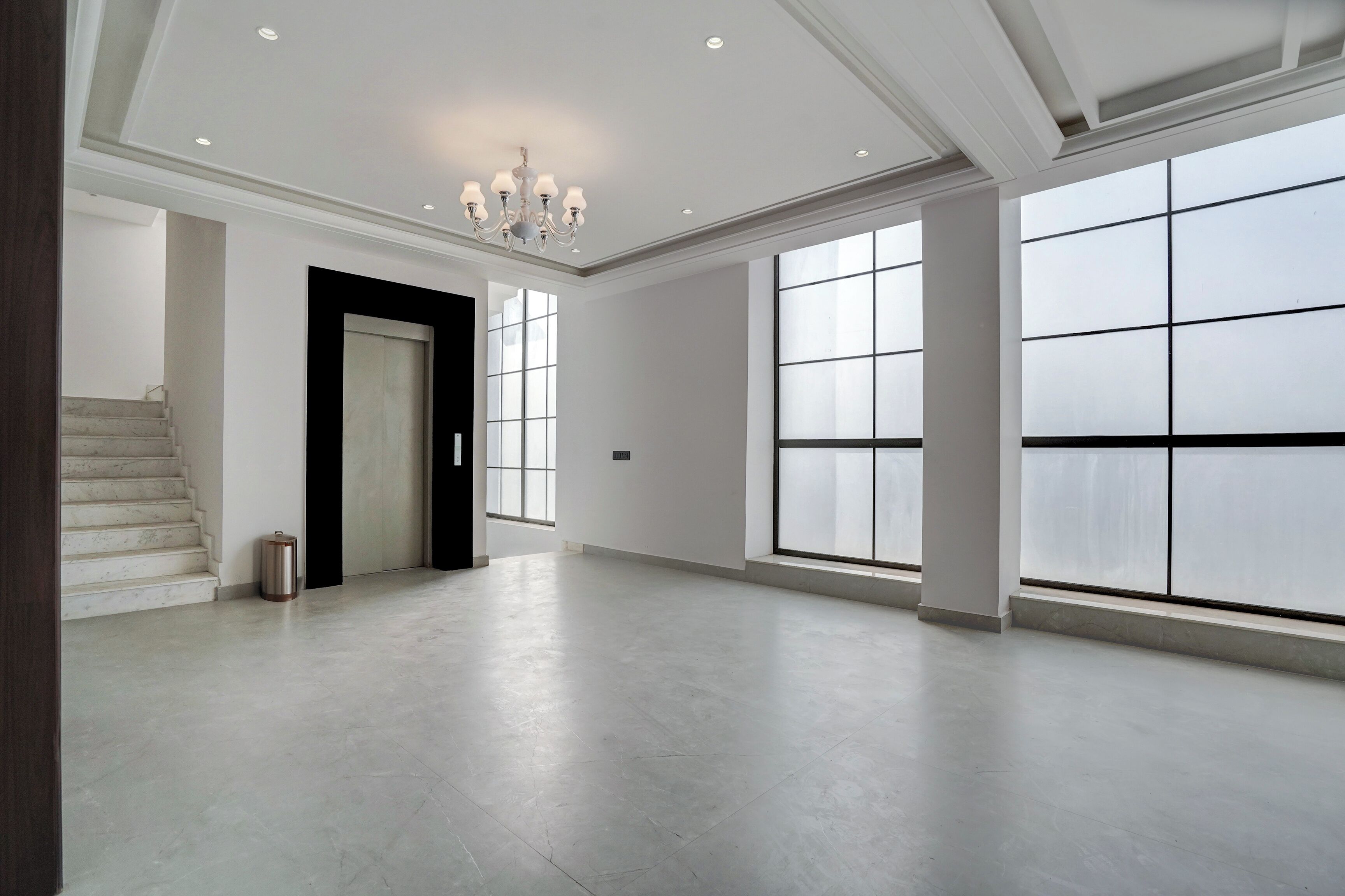 A spacious, well-lit room with a large window, a chandelier, and a staircase.