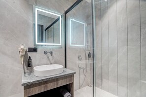 Un baño moderno con ducha acristalada, lavamanos blanco y un espejo grande con iluminación perimetral.