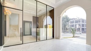 A modern hotel lobby with a glass partition, a staircase, and a view of a construction site outside. - Nirvana Hotel & Banquet (Batala)