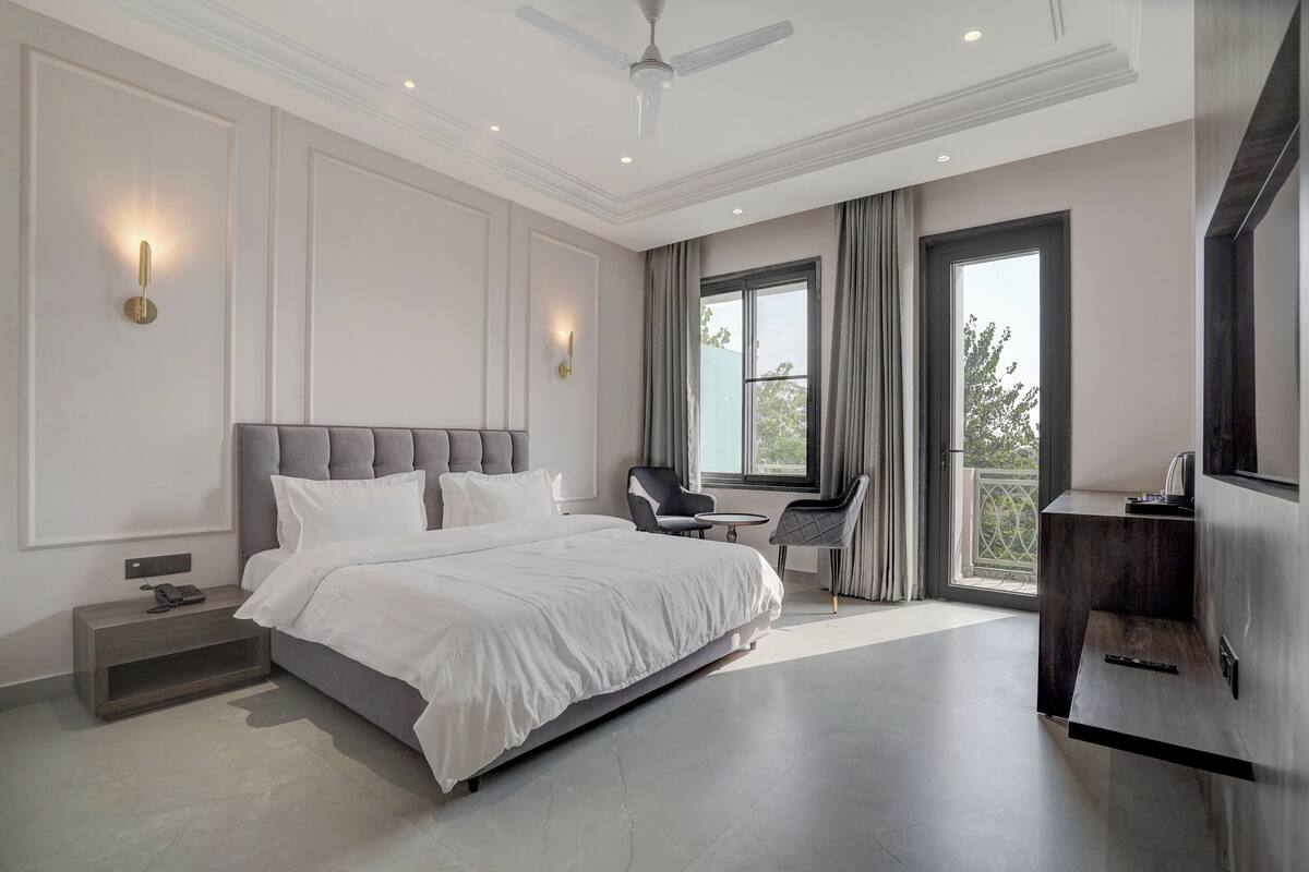 A modern bedroom with a large bed, a ceiling fan, and a view of the outdoors through a window.