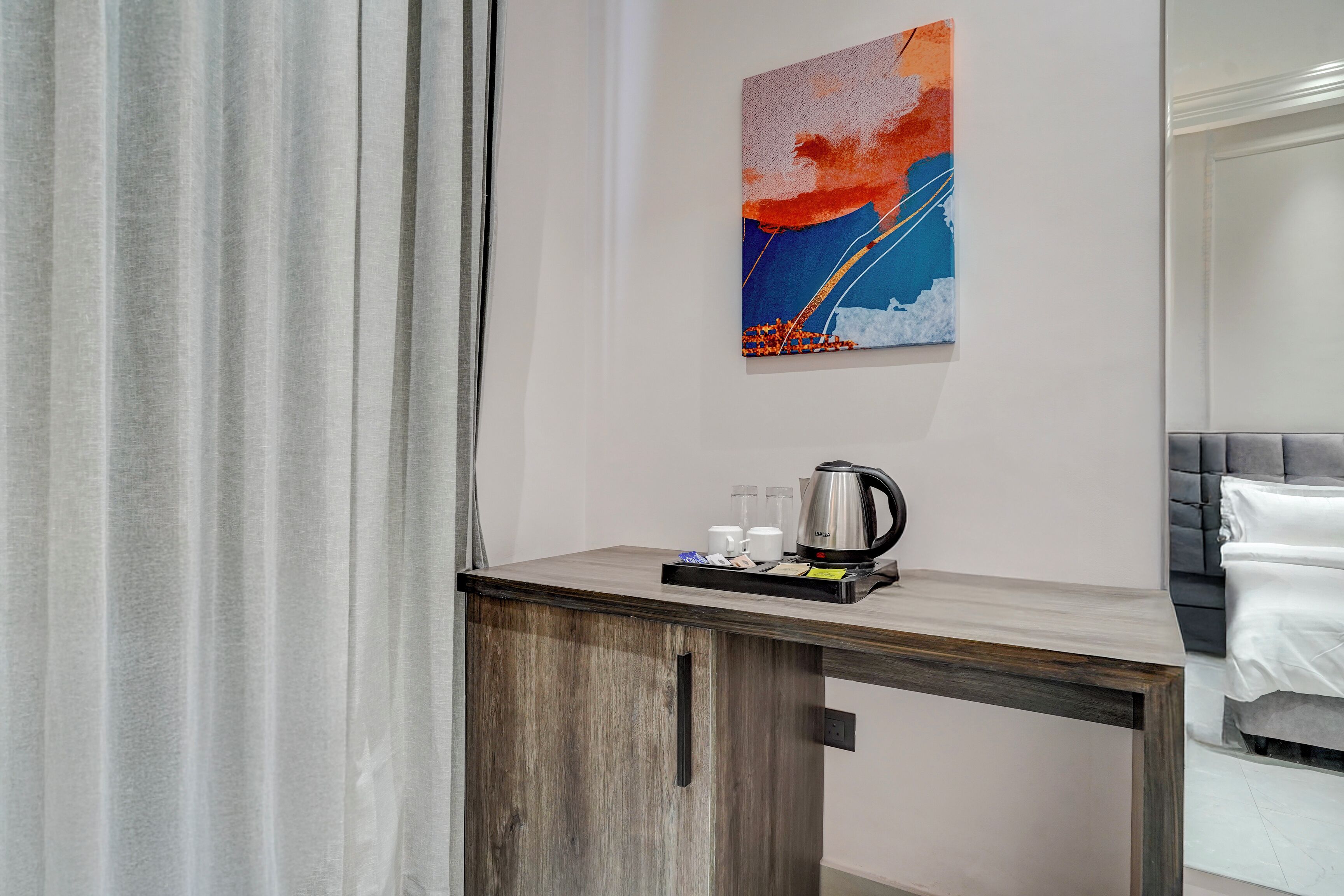Habitación de hotel con un escritorio de madera, un cuadro en la pared y una cama con cabecero gris.