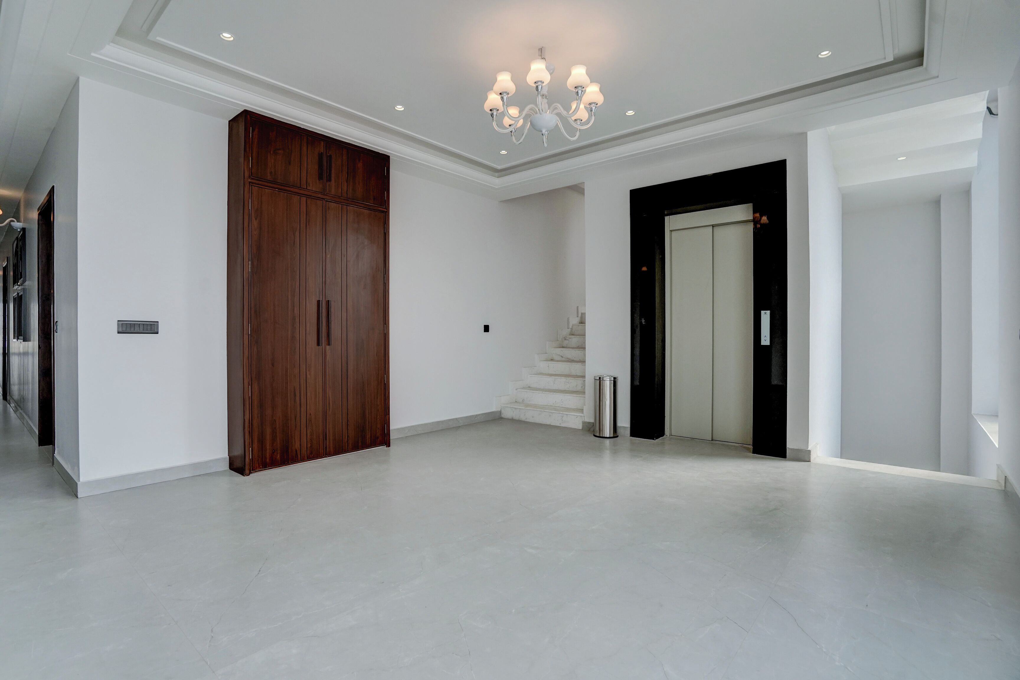 A spacious hallway with a wooden wardrobe, a staircase, and a modern chandelier.