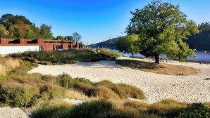 Une plage avec un grand arbre, un bâtiment avec un toit rouge et un ciel bleu dégagé.