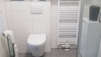A bathroom with a toilet, a towel dispenser, a shower, and a radiator.