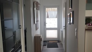 Un couloir avec un réfrigérateur noir, un meuble en bois, une porte avec une fenêtre et une porte avec un miroir.