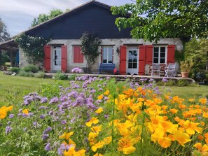 A house with a garden full of flowers, red shutters, and a blue chair outside. - Laurélie Cottage: A Haven of Serenity (Saint-Georges)