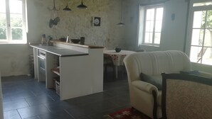 Una cocina con una isla central, un comedor con una mesa y un rincón de estar con una silla.
