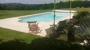 Una piscina con una sombrilla amarilla, rodeada de sillas de jardín y una planta en maceta.