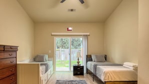 Ein Schlafzimmer mit zwei Betten, einem Schminktisch, einem Deckenventilator und einer Glasschiebetür, die in einen Garten führt.