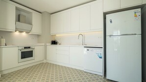Una cucina moderna con mobili bianchi, forno integrato, lavastoviglie e frigorifero.