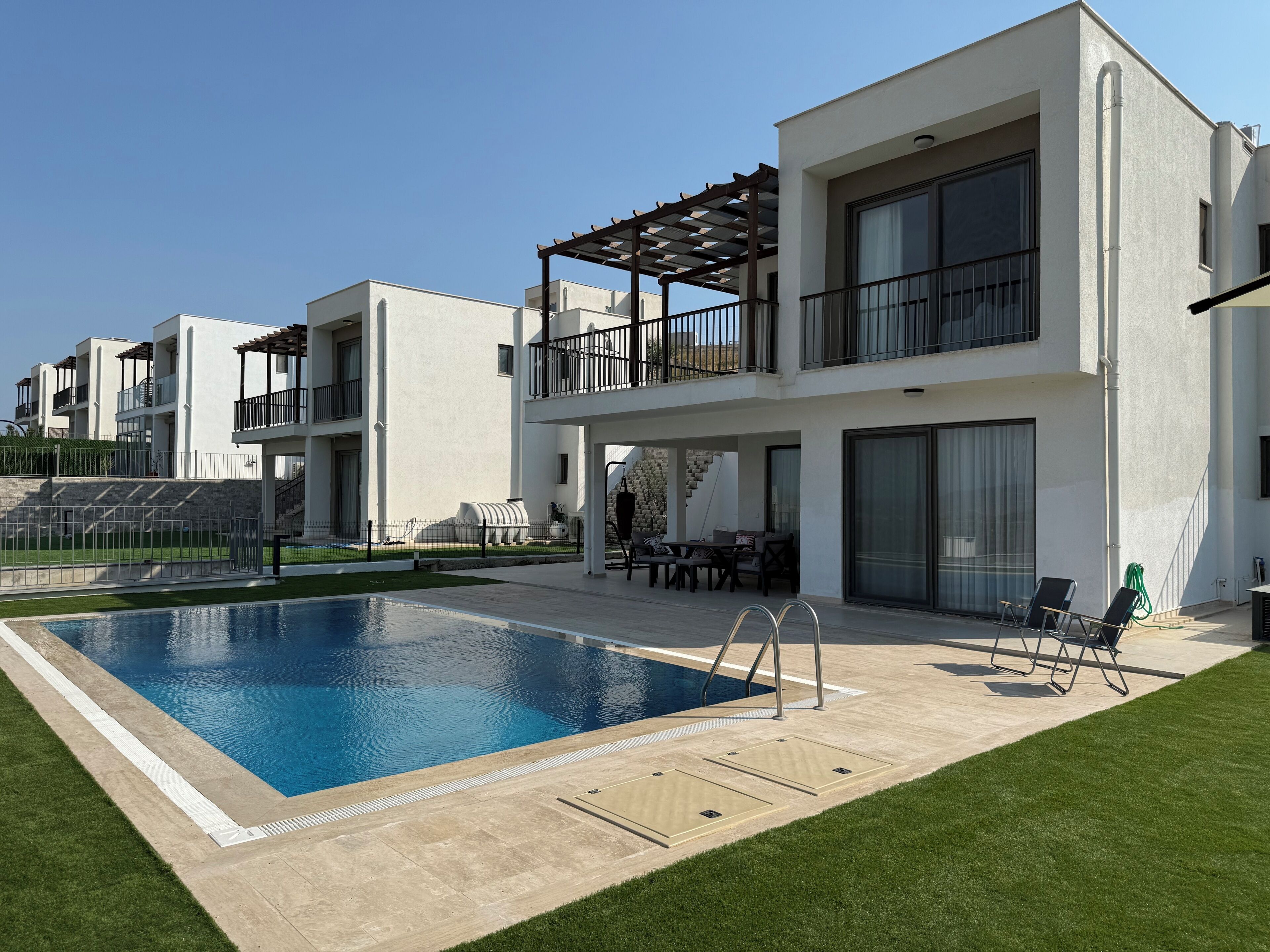 A modern residential building with a swimming pool, outdoor seating, and a covered patio area.