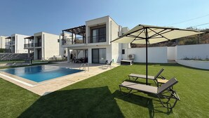 Una moderna casa a due piani con piscina, area salotto esterna e portico coperto.