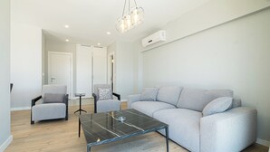Un soggiorno moderno con un divano grigio, due poltrone, un tavolino con piano in vetro e un lampadario.