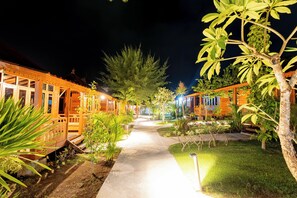 A pathway leading to a row of wooden cabins with a well-lit garden area. - Westwood Bungalow (Gili Trawangan)