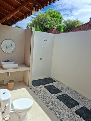 Een kleine badkamer met een wit wastafel, toilet en douchegedeelte, met een betegelde vloer met zwarte en witte kiezelstenen.