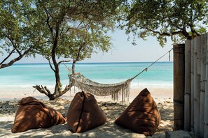 A hammock tied between trees on a sandy beach with a view of the ocean. - Westwood Bungalow (Gili Trawangan)
