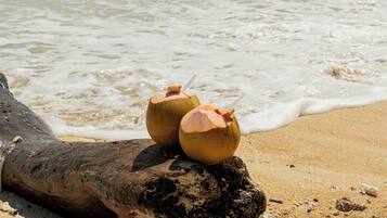 Two coconut drinks on a log by the beach.
