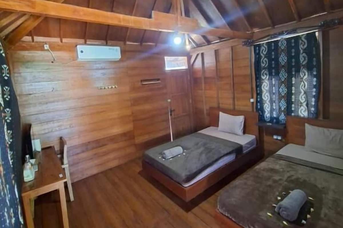 A wooden cabin room with a loft bed, a small desk, and a window with patterned curtains.