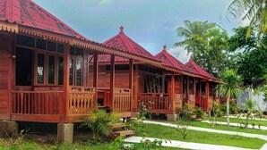 A row of wooden cabins with red roofs, each featuring a balcony and surrounded by greenery. - Westwood Bungalow (Gili Trawangan)