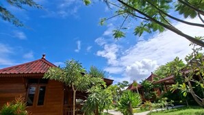A wooden house with a red roof, surrounded by lush greenery and a clear blue sky. - Westwood Bungalow (Gili Trawangan)