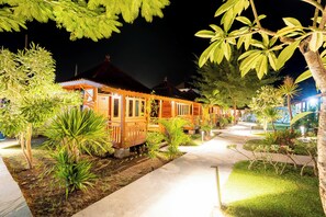 A wooden building with a porch, surrounded by tropical plants and a well-lit pathway. - Westwood Bungalow (Gili Trawangan)