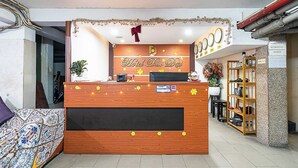 Balcão de recepção de hotel com acabamento em madeira, uma tela digital e uma placa com a inscrição "Hotel Didi Dat".