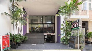 A entrada de um hotel com uma escadaria que leva à entrada, cercada por plantas em vasos e uma placa.