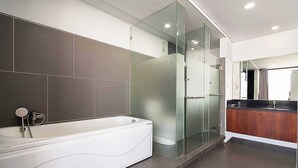Uma casa de banho moderna com uma banheira independente, um chuveiro com parede de vidro e uma toucador de madeira com espelho.
