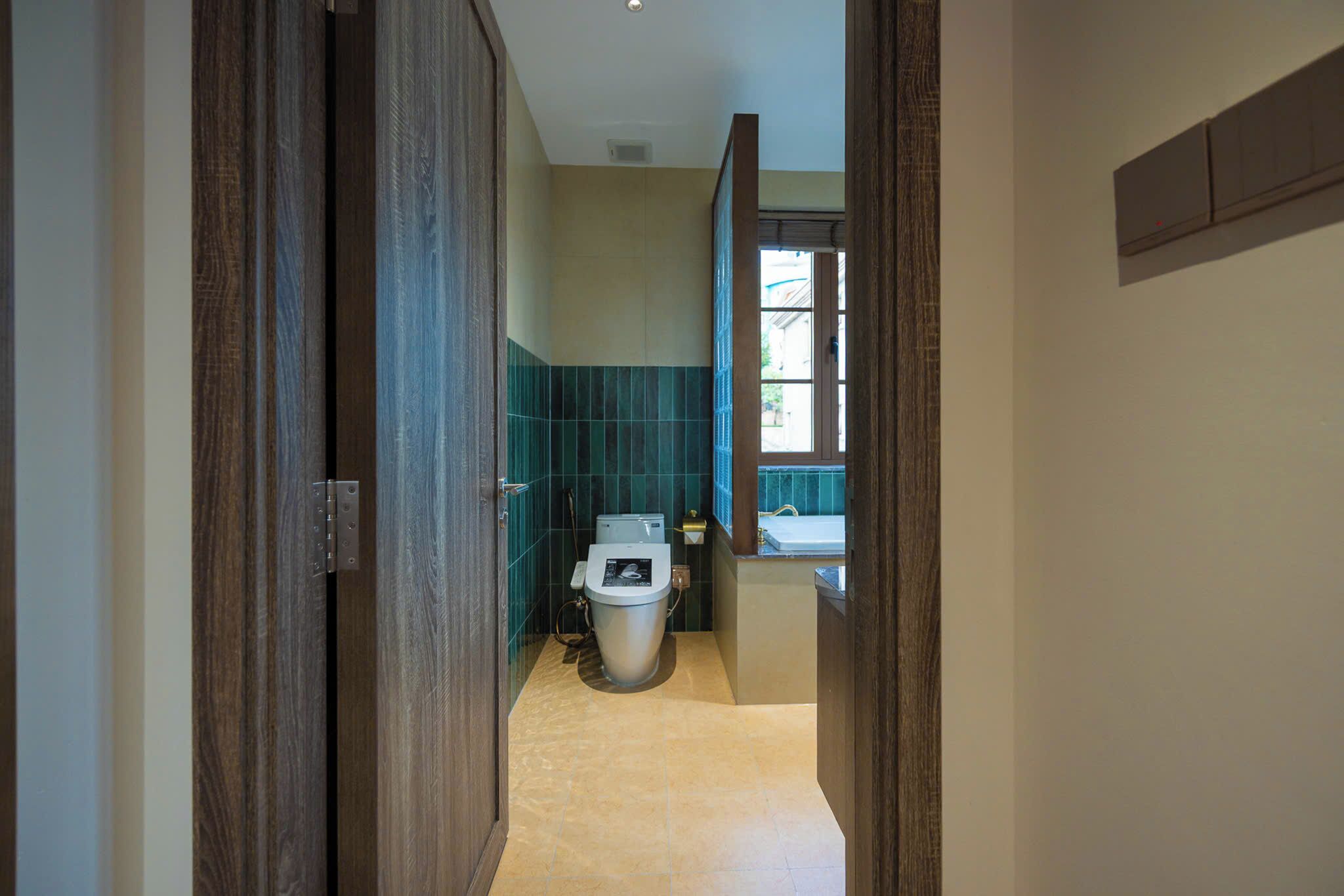 A narrow hallway leading to a bathroom with a toilet, sink, and a window.