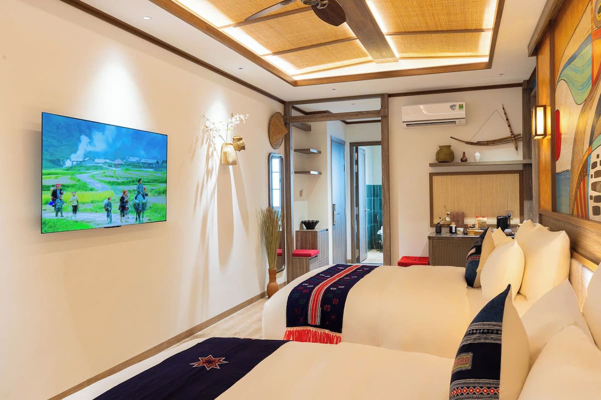 A hotel room with a large bed, a flat-screen TV mounted on the wall, and a view of the kitchen area.