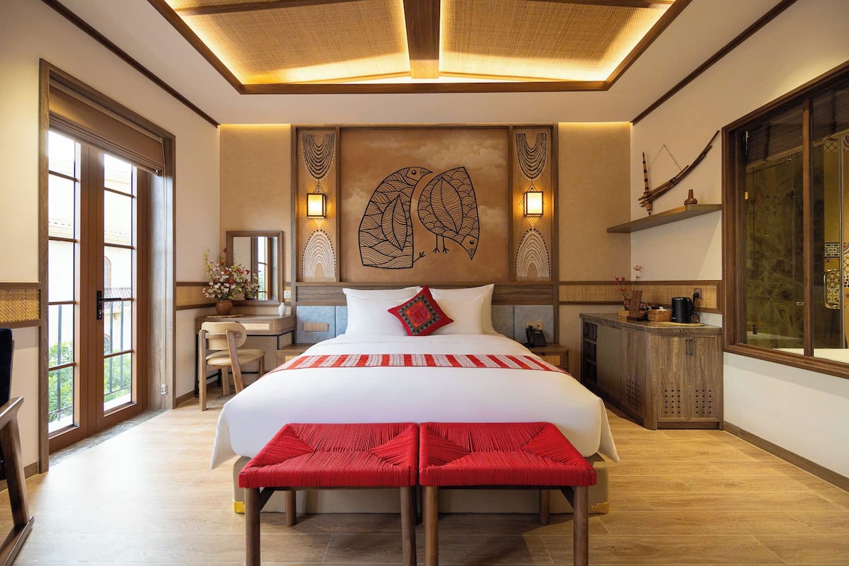 A spacious bedroom with a large bed, a desk, and a chair, a wooden cabinet, and a large window.