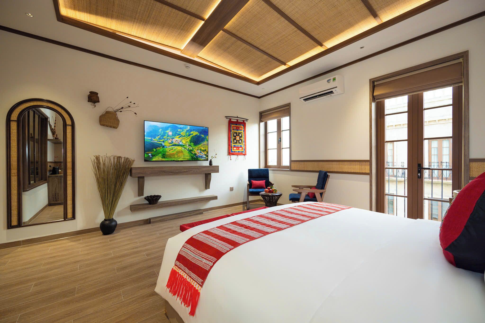 Una camera d'hotel con un letto grande, una TV a schermo piatto, un pavimento in legno, uno specchio, uno scaffale, una sedia e una finestra.