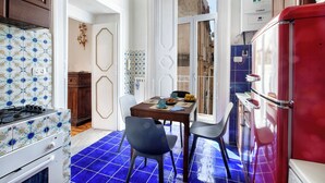 A compact kitchen with a red refrigerator, a stove, and a dining area with chairs and a table. - Teresella Suite (Naples)