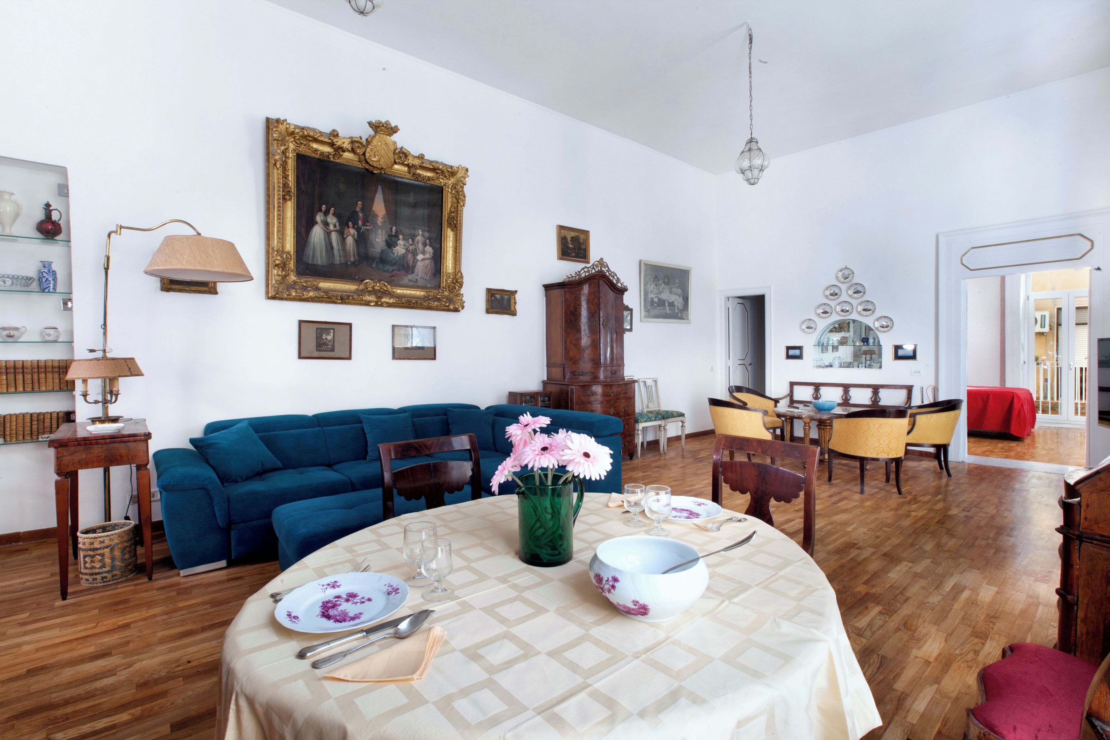 Un coin repas avec une table ronde dressée pour quatre personnes, un canapé bleu et un grand tableau encadré accroché au mur.