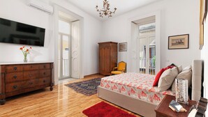 A spacious bedroom with a large bed, wooden dresser, and a television on the wall. - Teresella Suite (Naples)