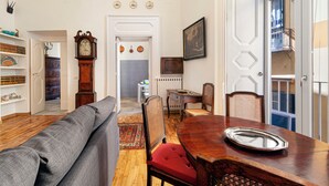 A dining area with a wooden table, chairs, and a sofa. There is a clock and a framed picture on the wall. - Teresella Suite (Naples)