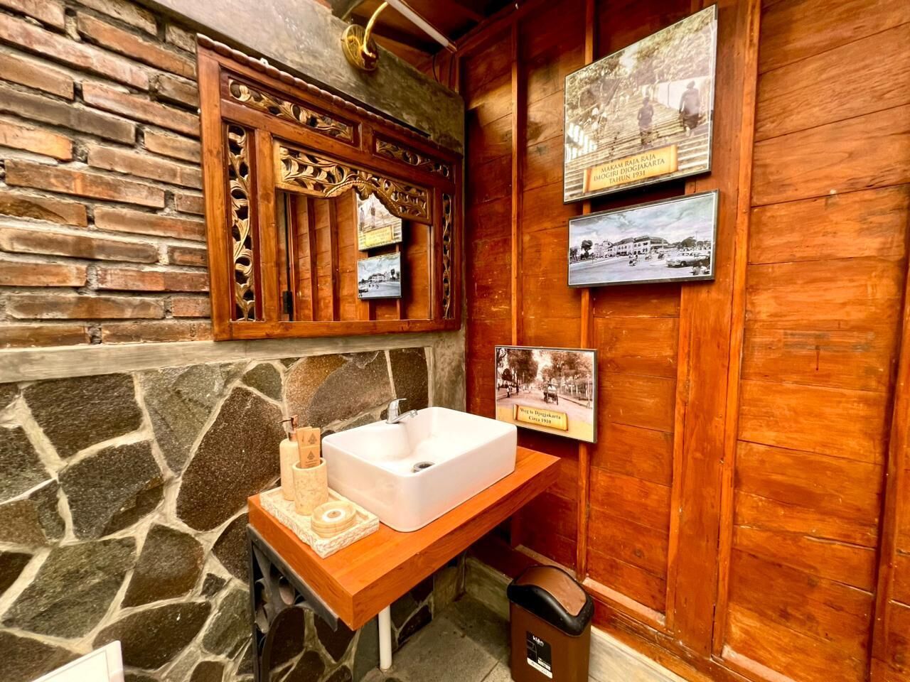 A bathroom with a stone wall, wooden paneling, a white sink, and historical photos on the wall.