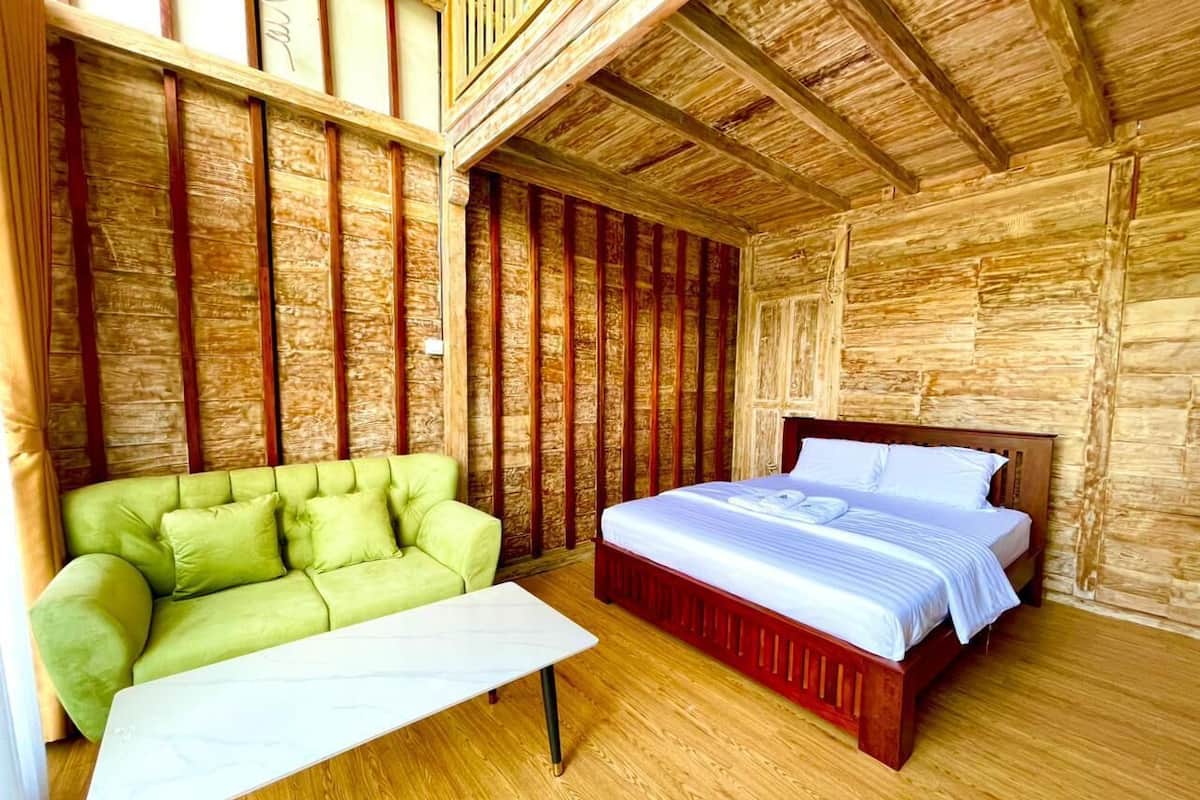 A room with a wooden ceiling, a green sofa, a bed with white bedding, and a white table.