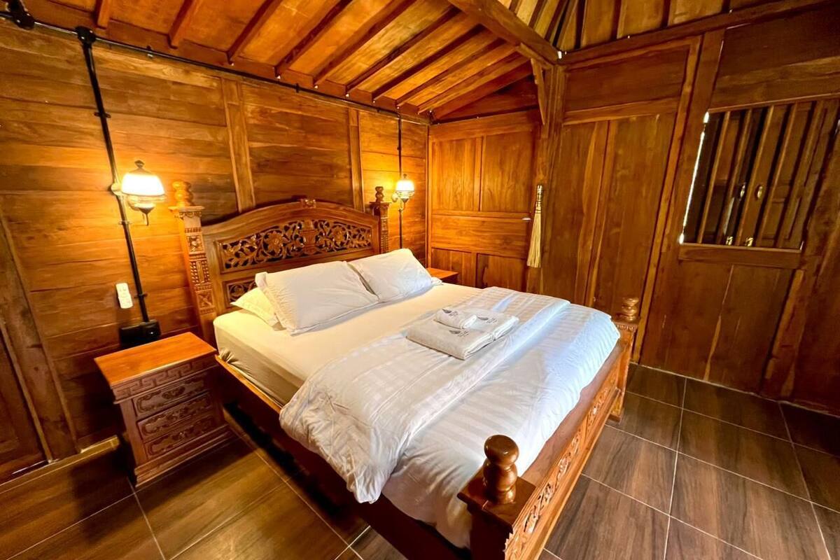 A wooden-paneled bedroom with a large bed, two bedside tables, and wall-mounted lamps.