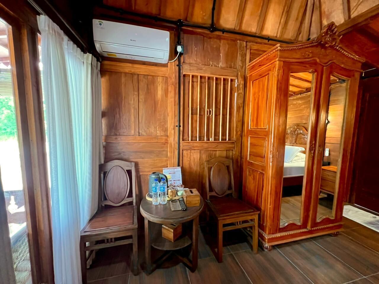 Una habitación de madera con una cama, una mesa con botellas de agua, una silla y un equipo de aire acondicionado.