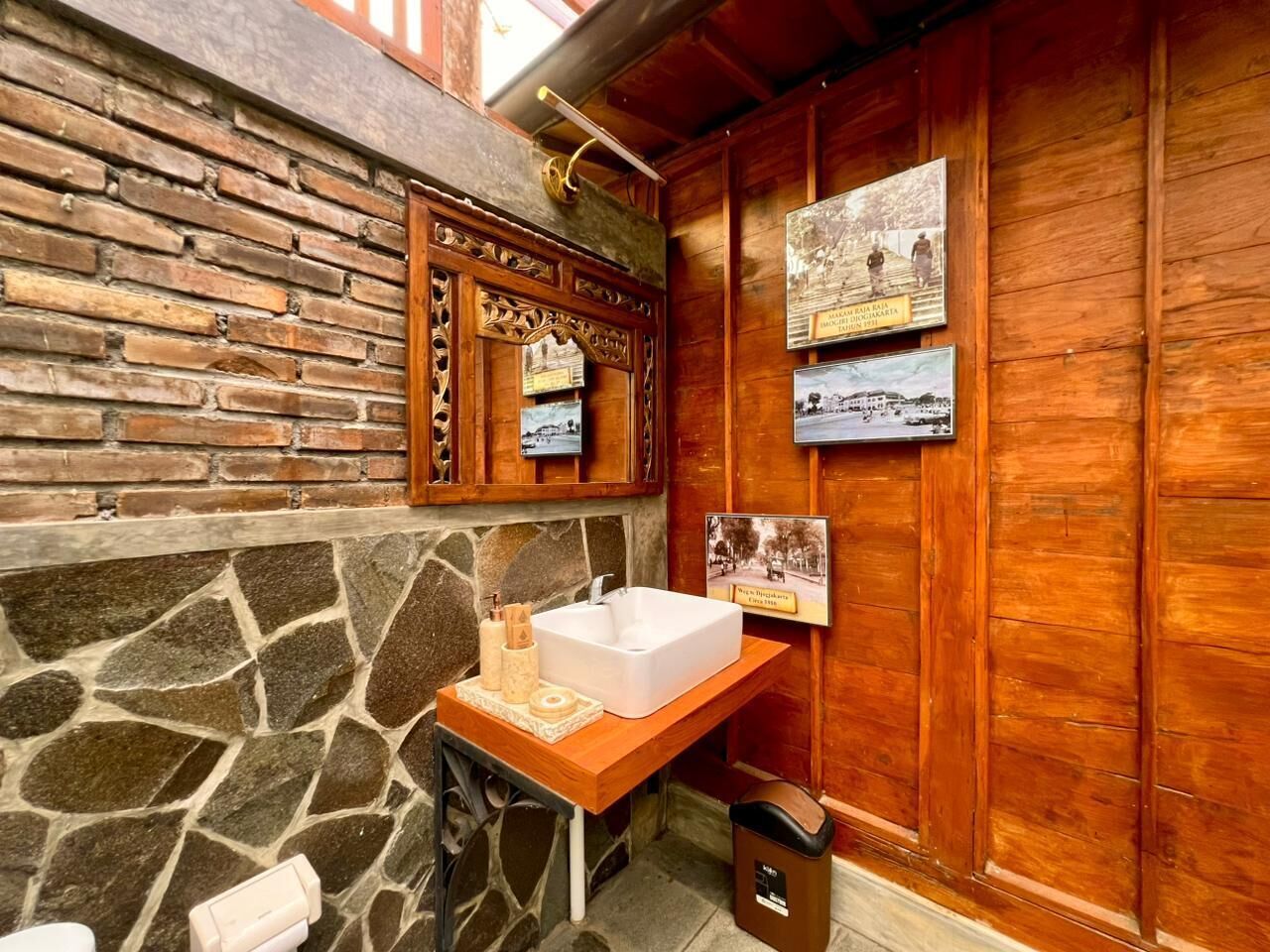 Un baño con pared de piedra, paneles de madera, un lavabo blanco y fotografías históricas en la pared.